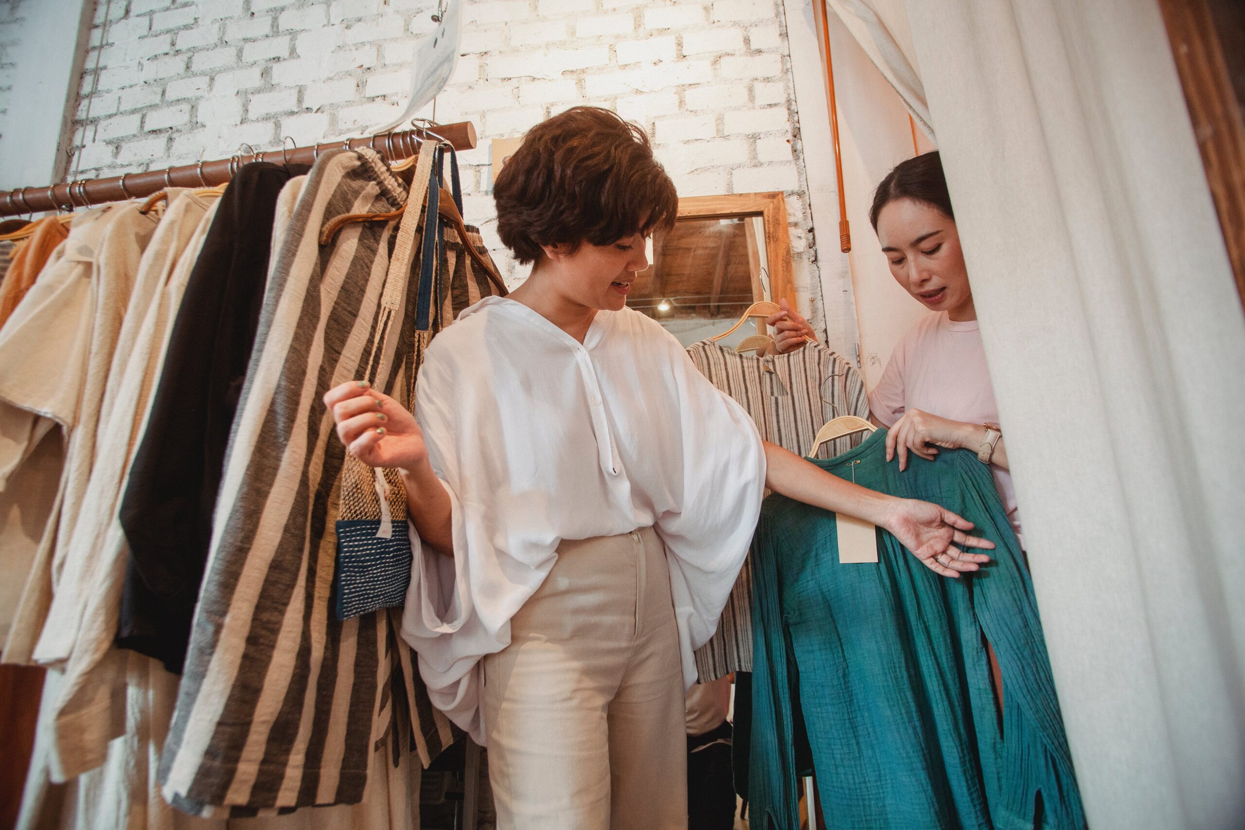 Mulher mostrando peças de roupas para cliente em loja