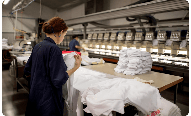 Mulher dobrando peças de roupas em confecção